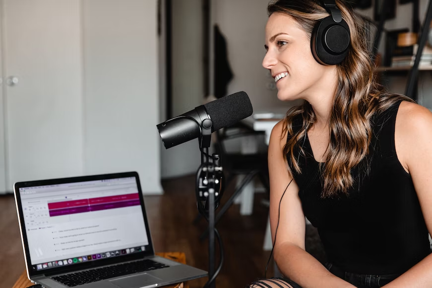 Woman speaking into a microphone and laptop for a podcast or radio broadcast - outbound marketing - Shift4Shop