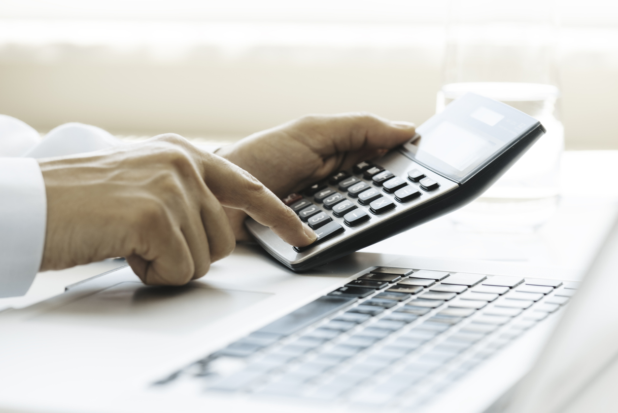 Man calculating customer acquisition cost on a calculator in front of a laptop - Shift4Shop