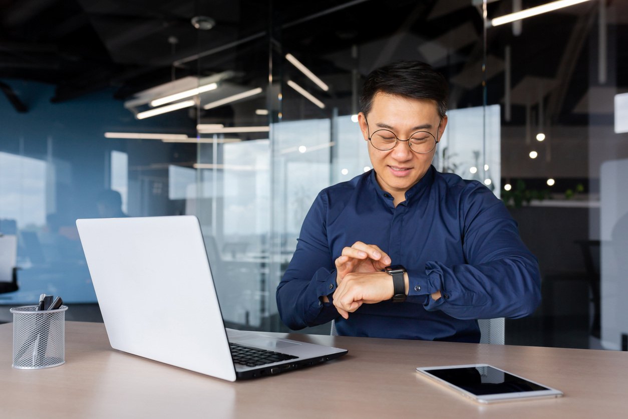 Business owner on a laptop looking at his watch determining the right frequency for sending emails to eCommerce customers | Shift4Shop